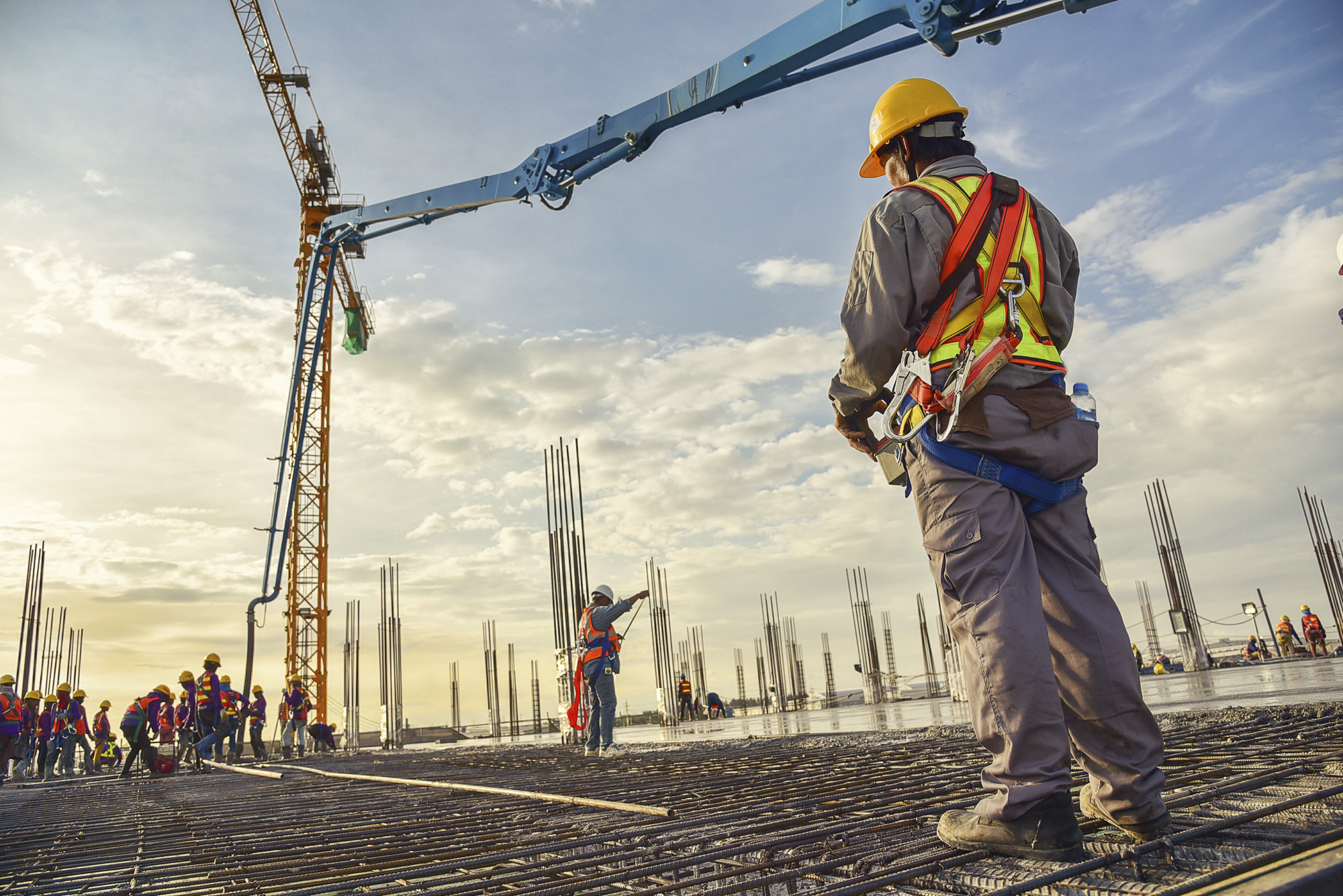 A construction worker control a pouring concrete pump on constru Construction workers on site wearing safety gear, with a crane in the background, emphasizing OSHA compliance and safety training in a construction environment.