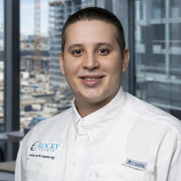 Smiling safety consultant in Rocky Zapata uniform, with city skyline in background, representing occupational safety expertise and corporate commitment.