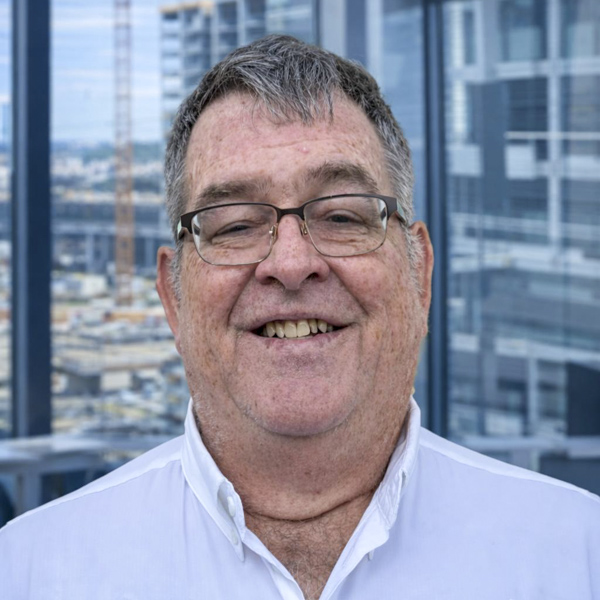 Smiling man in glasses wearing a white shirt, with a cityscape background, representing Rocky Zapata Safety Consultants.