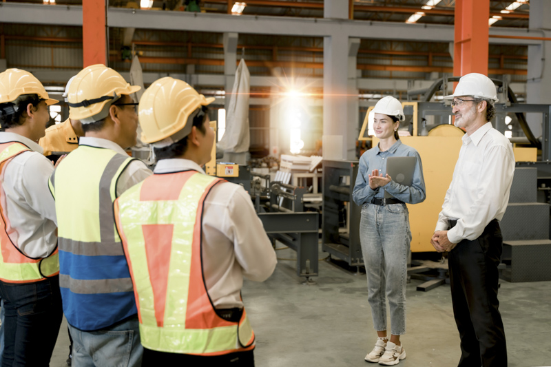 woman worker and engineer under inspection and checking producti Group of construction professionals in safety gear discussing safety protocols in an industrial setting, emphasizing safety consulting and OSHA compliance.