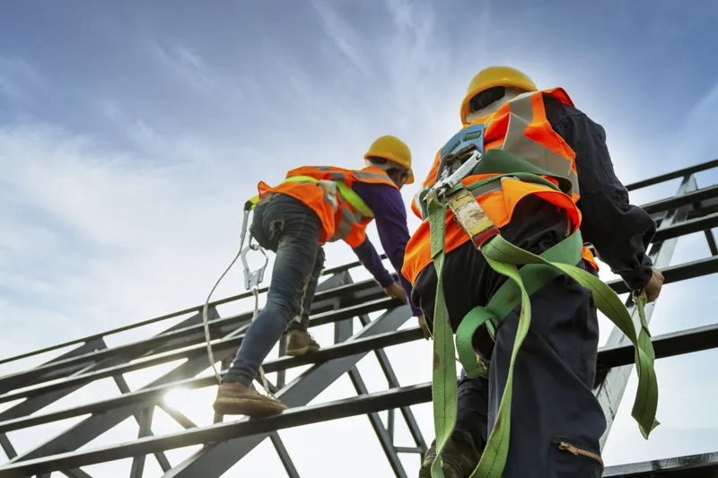 Construction workers wearing safety harnesses and vests on a rooftop, demonstrating workplace safety and emergency preparedness.